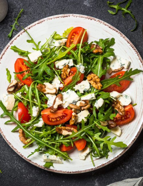 Arugula salad with tomatoes, blue cheese and walnuts. Healthy vegetarian dish. Top view image.