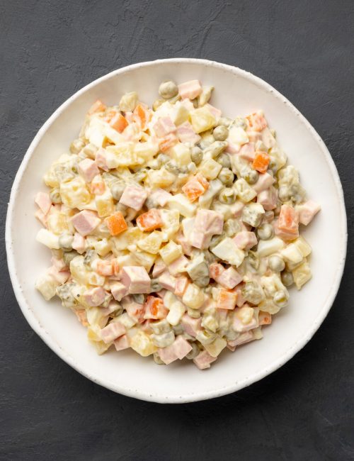 Russian salad Olivier with mayonnaise on plate. Black background. Top view, flat lay.